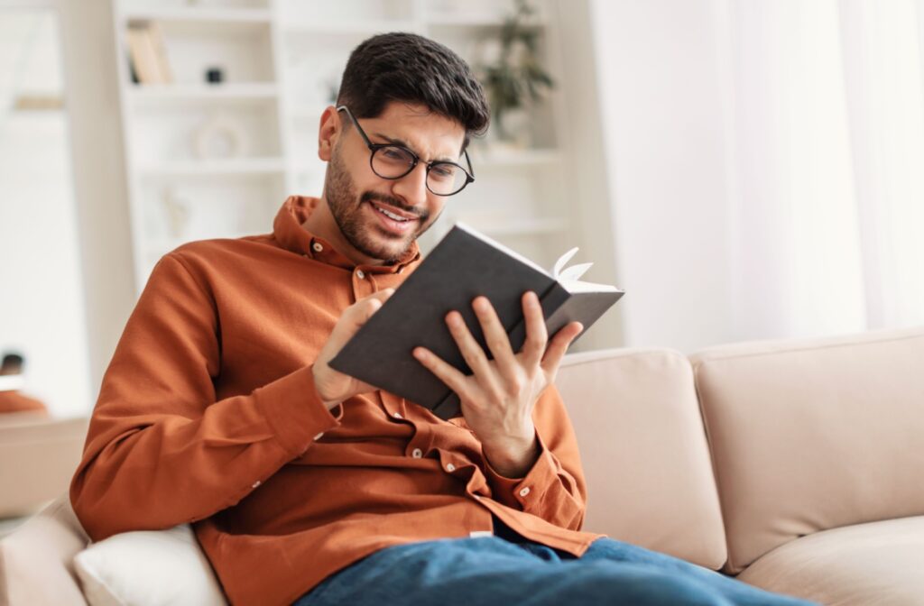 A man reading a book with the help of a pair of reading glasses.