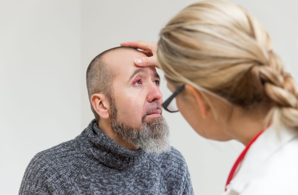 A female optometrist carefully examines a male patient's right eye to diagnose a stye.