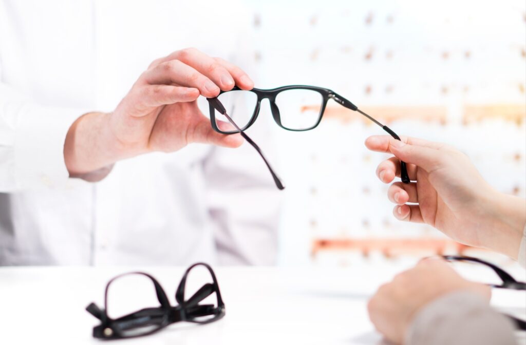 An optometrist handing an out-of-frame patient a pair of single-vision eyeglasses.