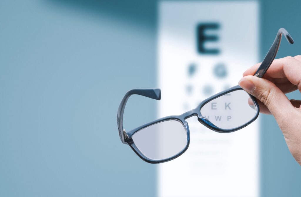 A person holding a pair of glasses in front of a Snellen chart, bringing the letters into focus with the corrective lenses.