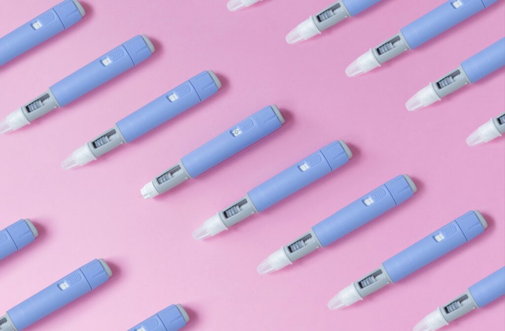 A bunch of ozempic injections lined up evenly on a pink background.