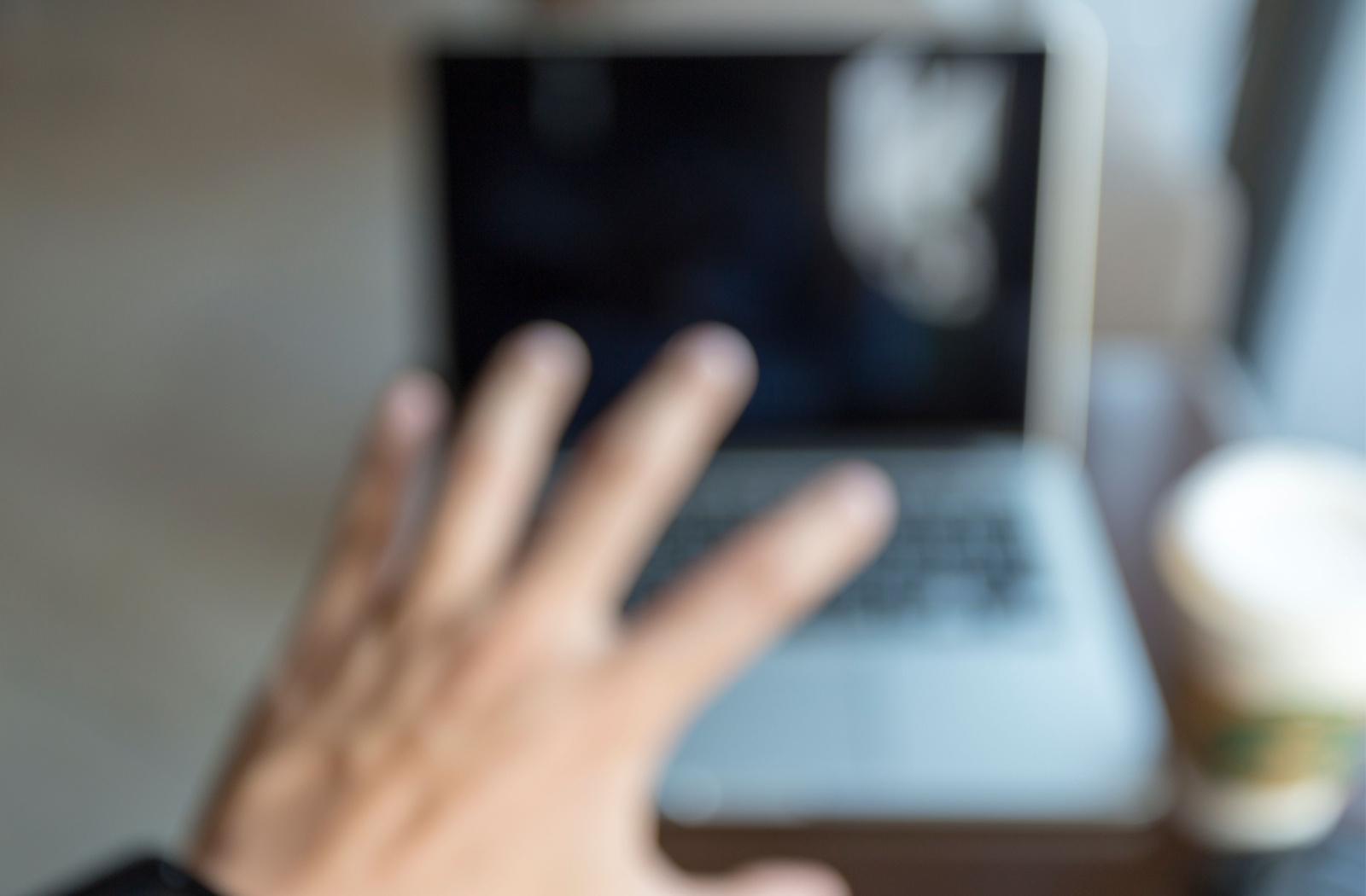 A perspective of someone with blurry vision, reaching their hand out in from of their laptop computer with a cup of coffee sitting next to the keyboard.