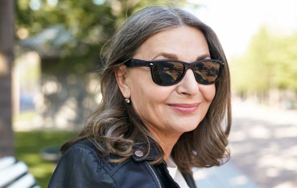 A close up of a person sitting on a bench outside, wearing polarized sunglasses.